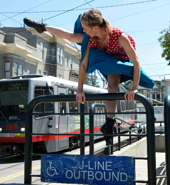 Woman performing dance move on J Line platform with light rail vehicle behind her.