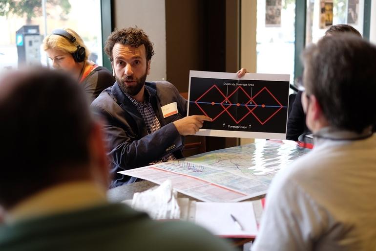Man presenting transit coverage diagram to seated audience members at table.