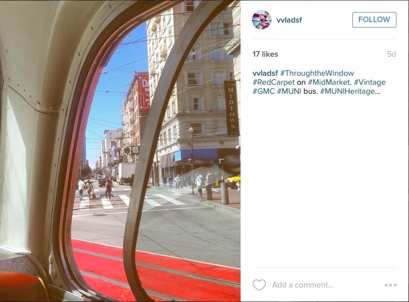 View through vintage streetcar window of Market Street with red carpet and city buildings.