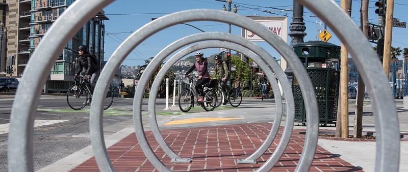 Bikers riding past a bike rack.
