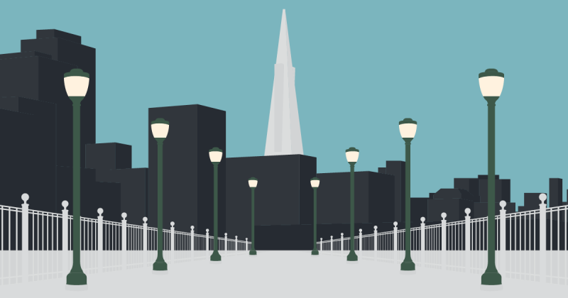 Looking landward from the walkway of Pier 7. The walkway is flanked by old-style green streetlamps, all lit. In the background are dark office buildings a light gray Transamerica pyramid.