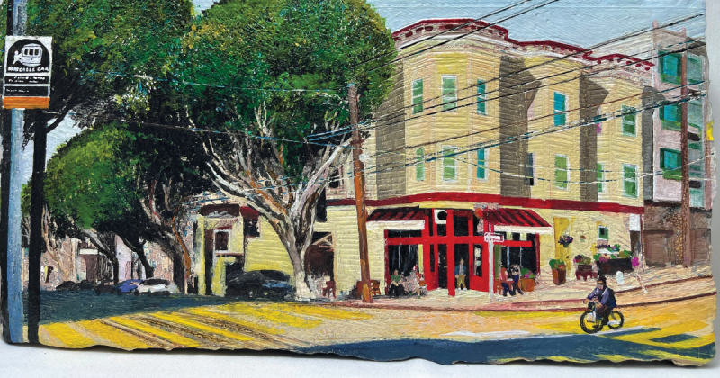An intersection in Nob Hill with cable car tracks and a cable car stop sign. There are trees and an older yellow three-story building. A person on a bicycle enters the intersection. People sit or walk outside the red storefront.