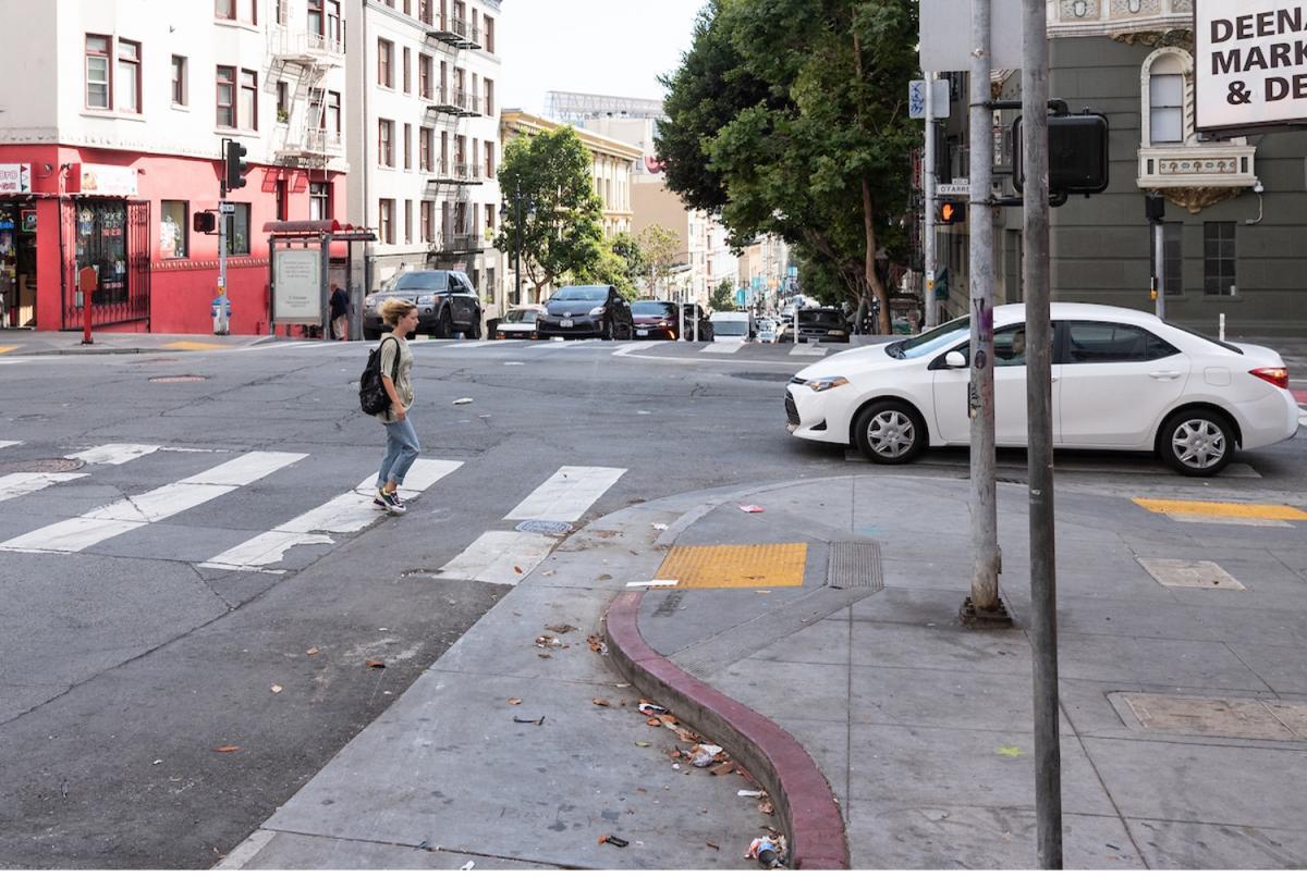 a pedestrian crosses the street at o'farrell, where there's a concrete bulb-out added to the sidewalk at the intersection