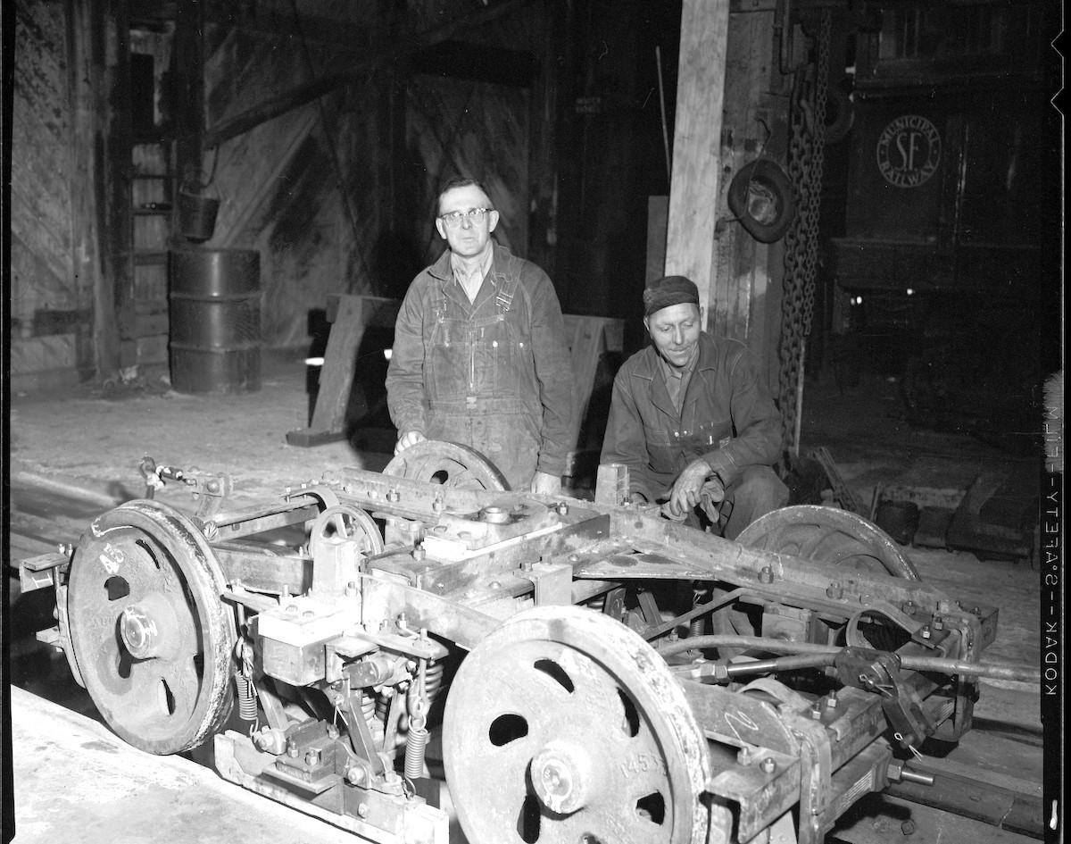  Two mechanics stop for a photo with an overhauled cable car truck