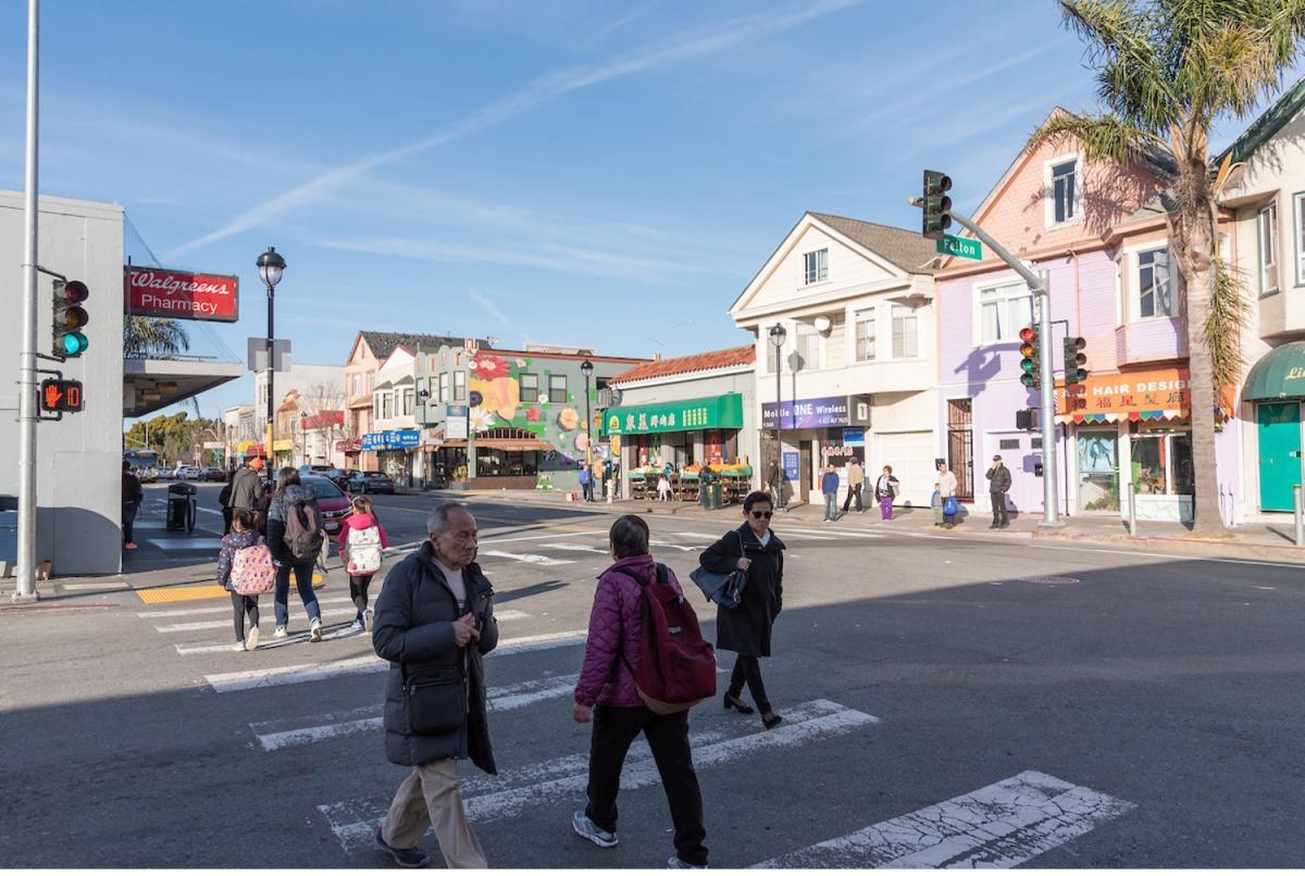 many pedestrians cross along a crosswalk; there's a countdown signal that displays an orange hand with 10 next to it