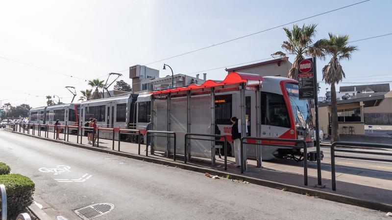 street-level transit platform with train and people waiting