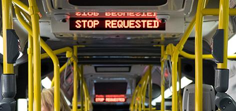 A passenger holds onto a stanchion for support during a bus ride Stantions and straps on a New Flyer bus. Stop Requested is displayed.