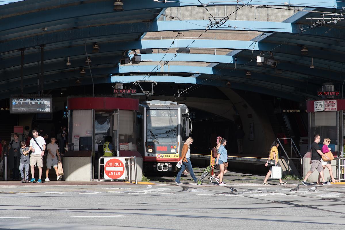 As a K Ingleside train waits to exit West Portal Station, people walk in the crosswalk in front of the station.