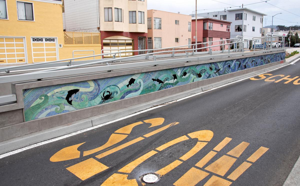 We see artwork on a new L Taraval accessible boarding platform with a freshly paved road beside it and the word "slow."