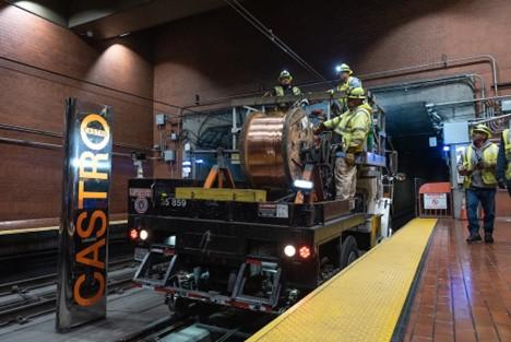 Workers on a truck in a subway station with a large roll of wiring