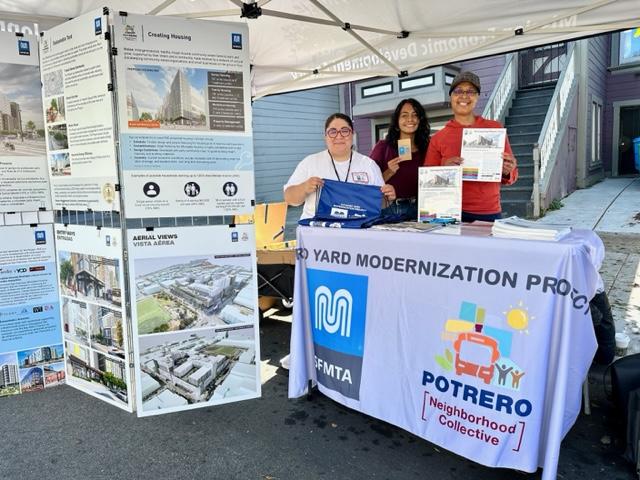 people under a tent canopy smile at the camera. they are surrounded with visual informational boards