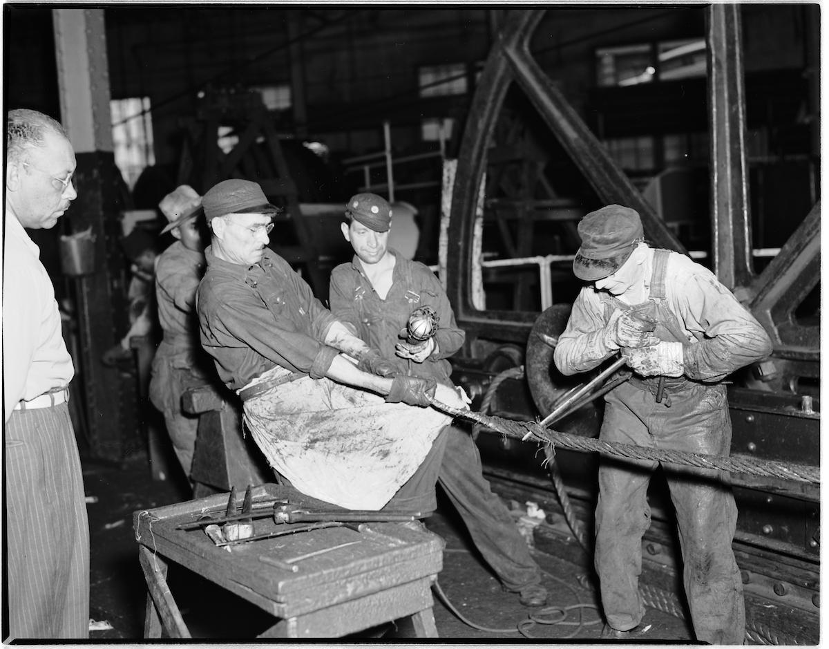 In a black and white photo, cable car repairers work together to splice a cable 