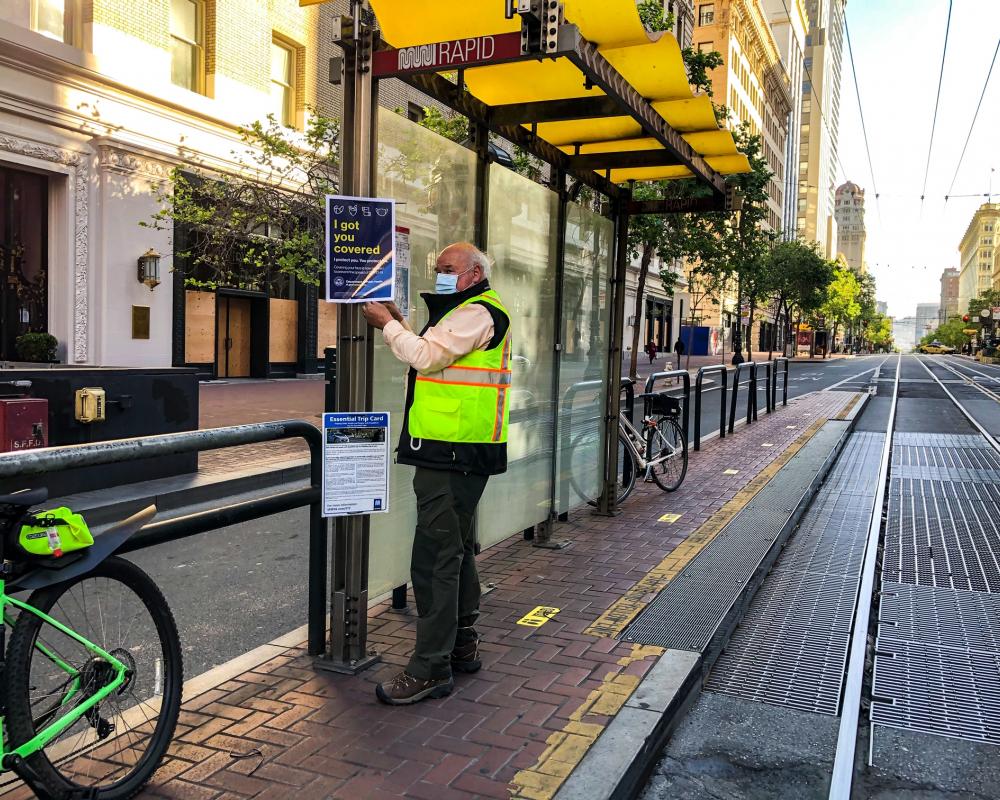 Photo of a Market Street Ambassador posting new face mask, ETC, and wayfinding signage on a boarding island bus stop.