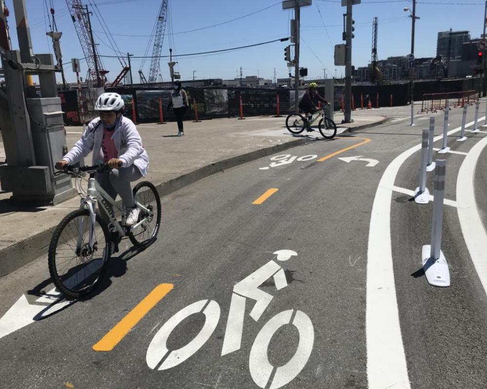 two people riding in a two-way protected bikeway that is marked by bicycle symbols on the roadway