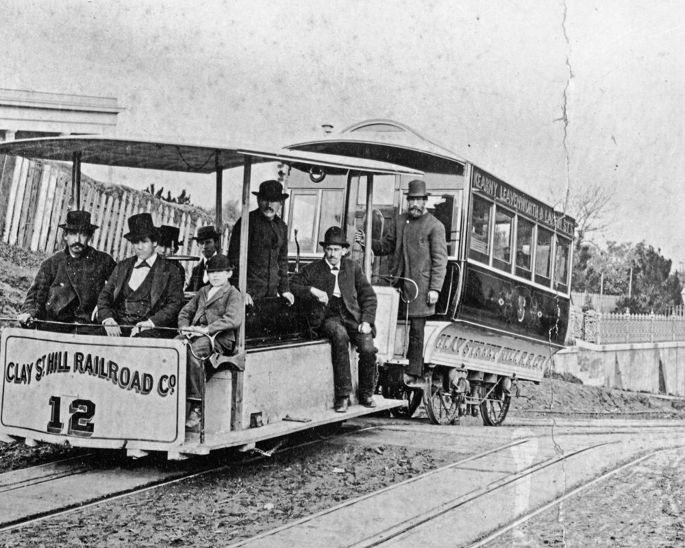 black and white photo of original cable train on clay street hill in 1873 with people on board.