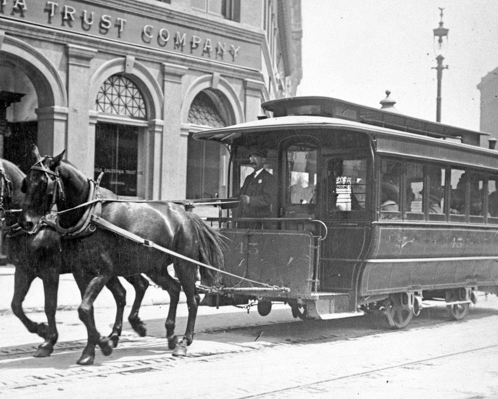black and white photo of a horse-drawn streetcar in downtown san francisco in the late 1800s.
