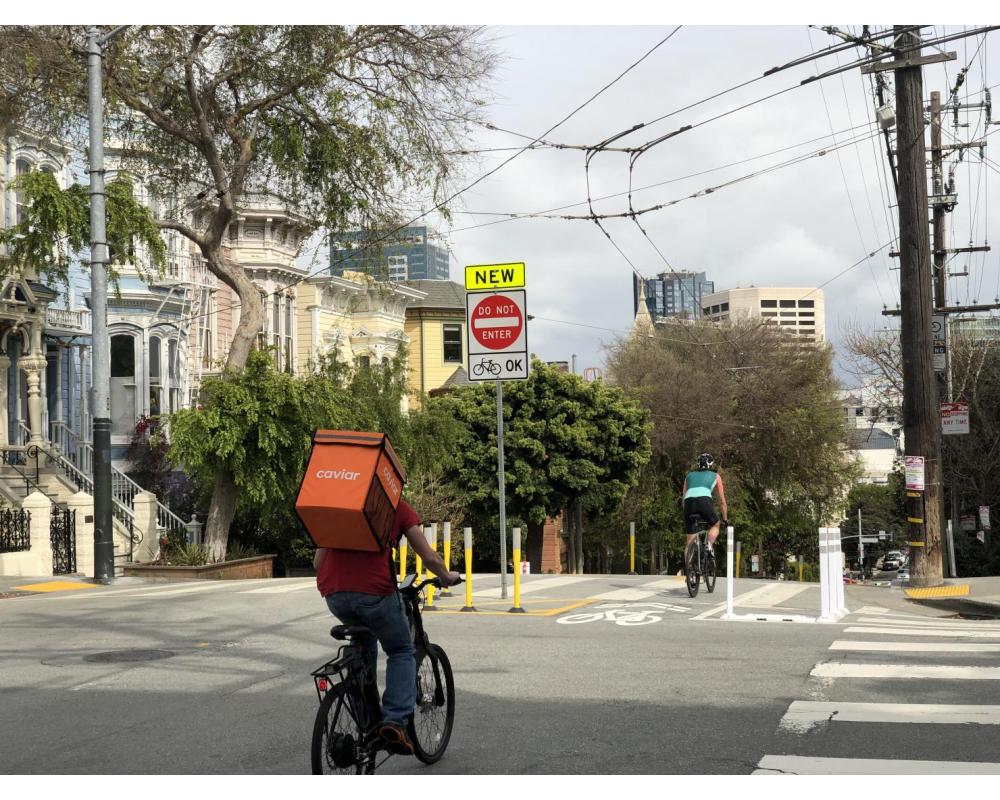 View of two people on bikes using the protected downhill bikeway on Page Street at Laguna Street, facing east toward Downtown