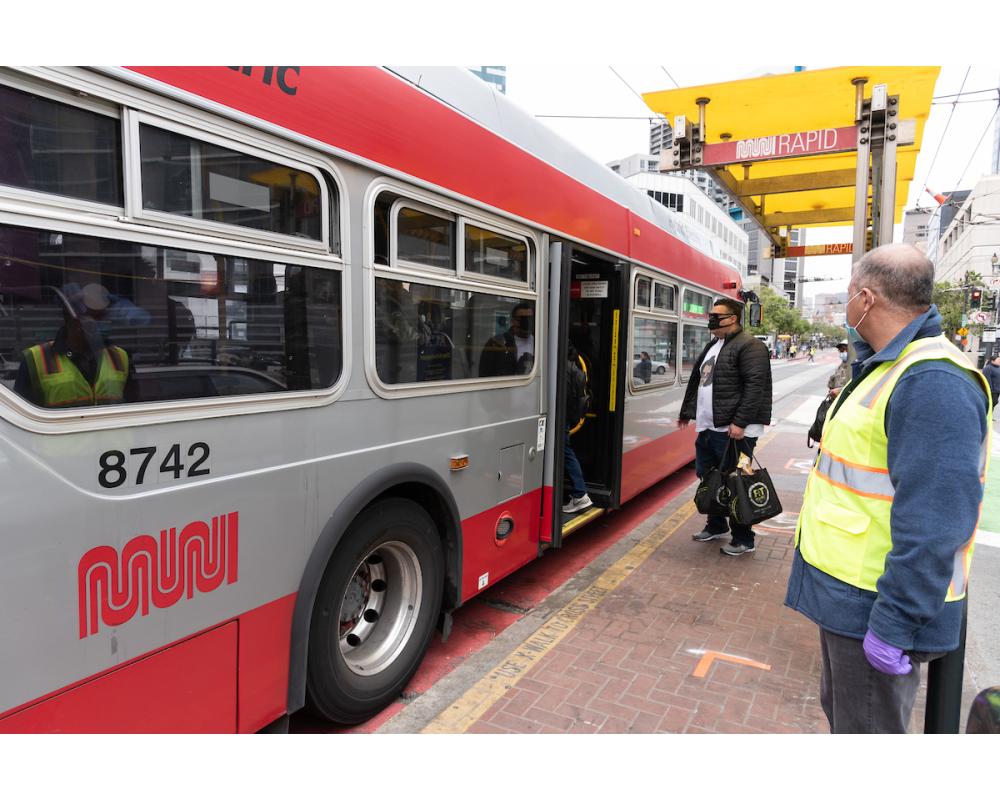 Muni Ambassador looks on as customer wearing a mask waits to board through the back after taking an essential trip for groceries