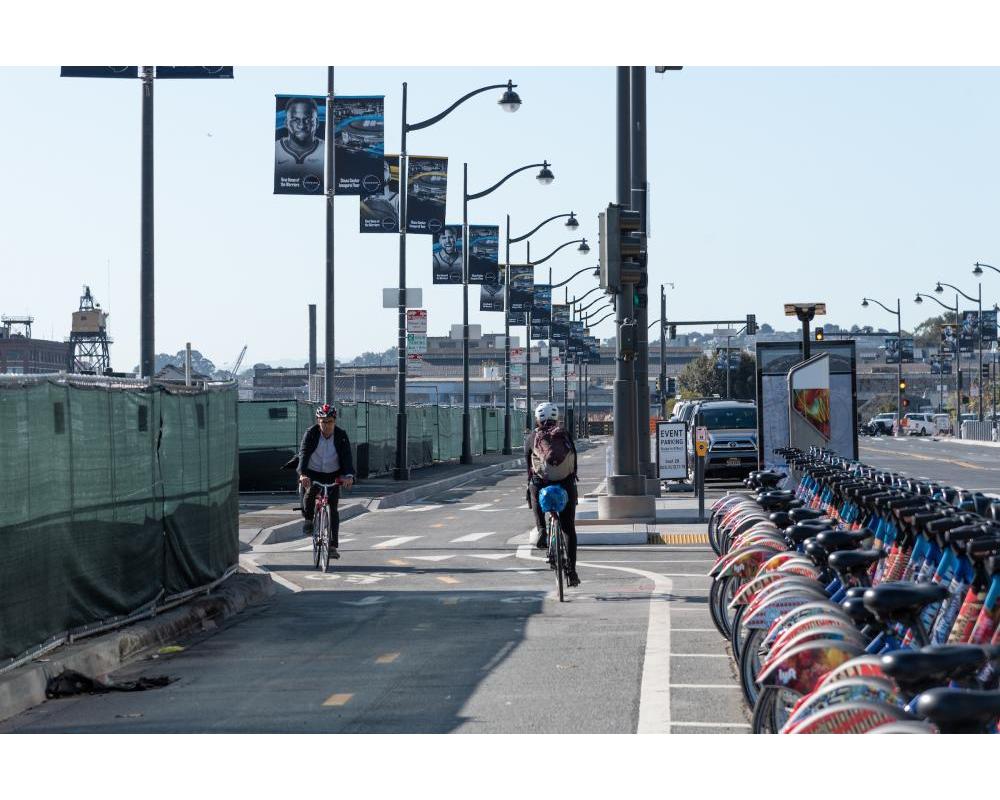 Two bicyclists in the two-way protected bikeway on Terry Francois Blvd. with a bikeshare station located in the buffer
