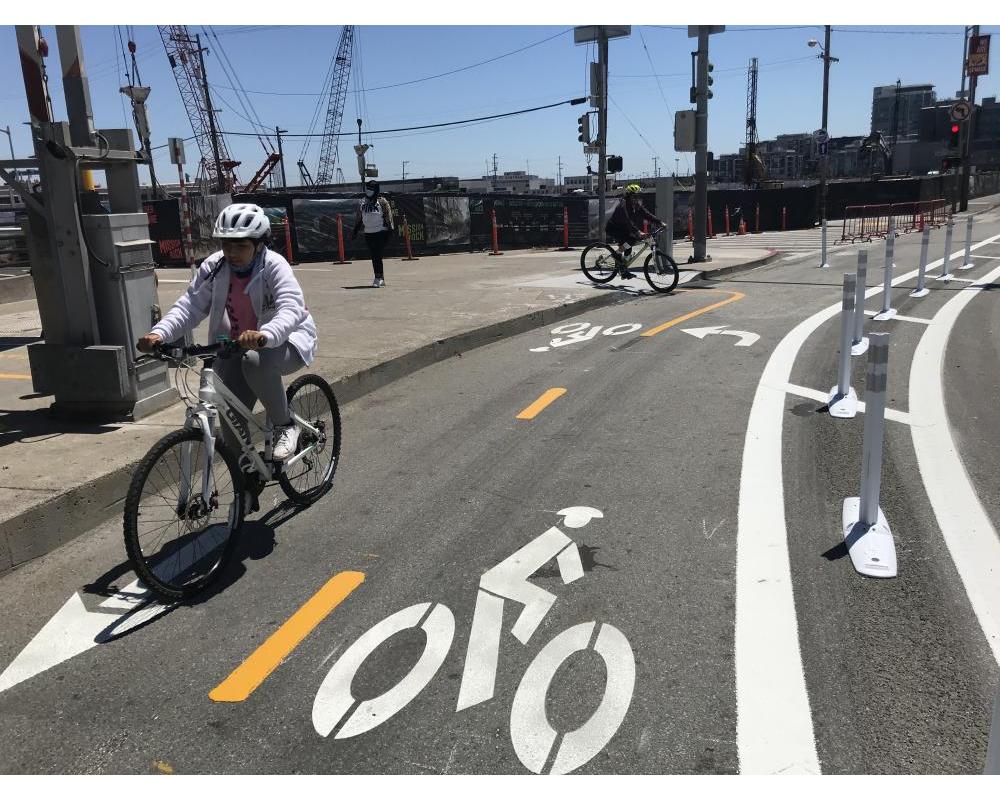 two people riding in a two-way protected bikeway that is marked by bicycle symbols on the roadway