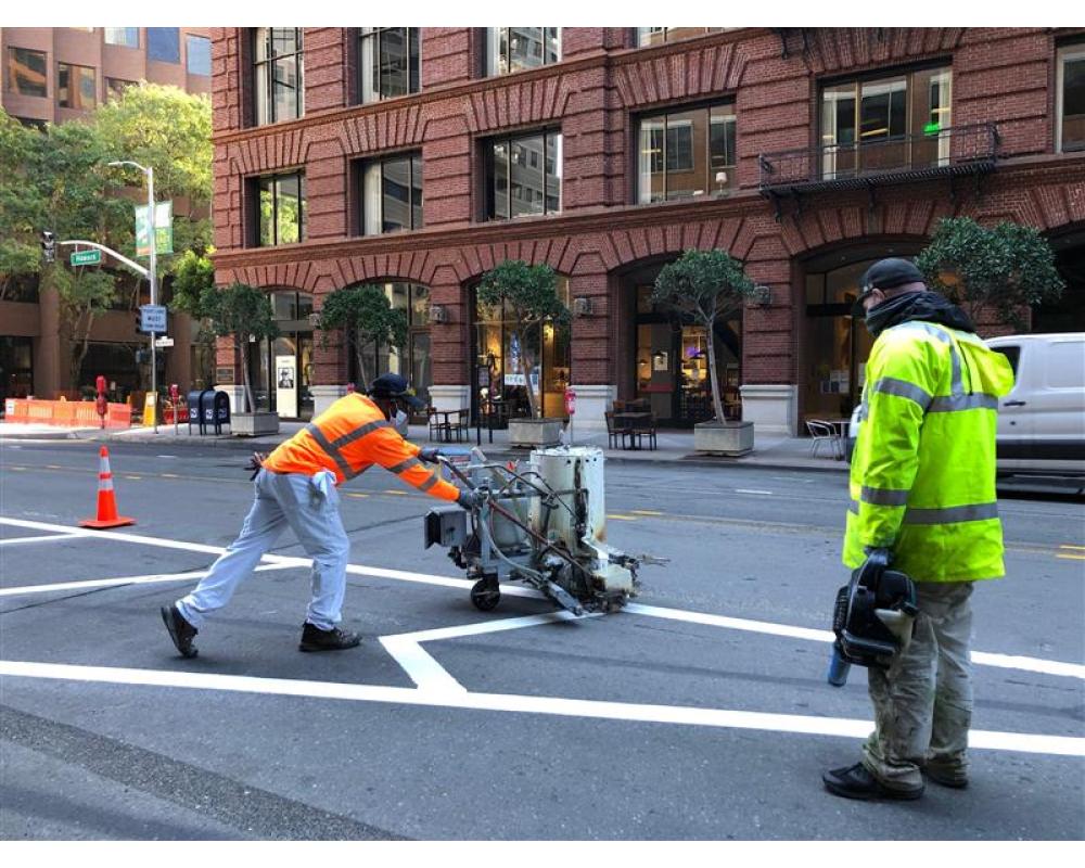 Two employees with equipment painting the road