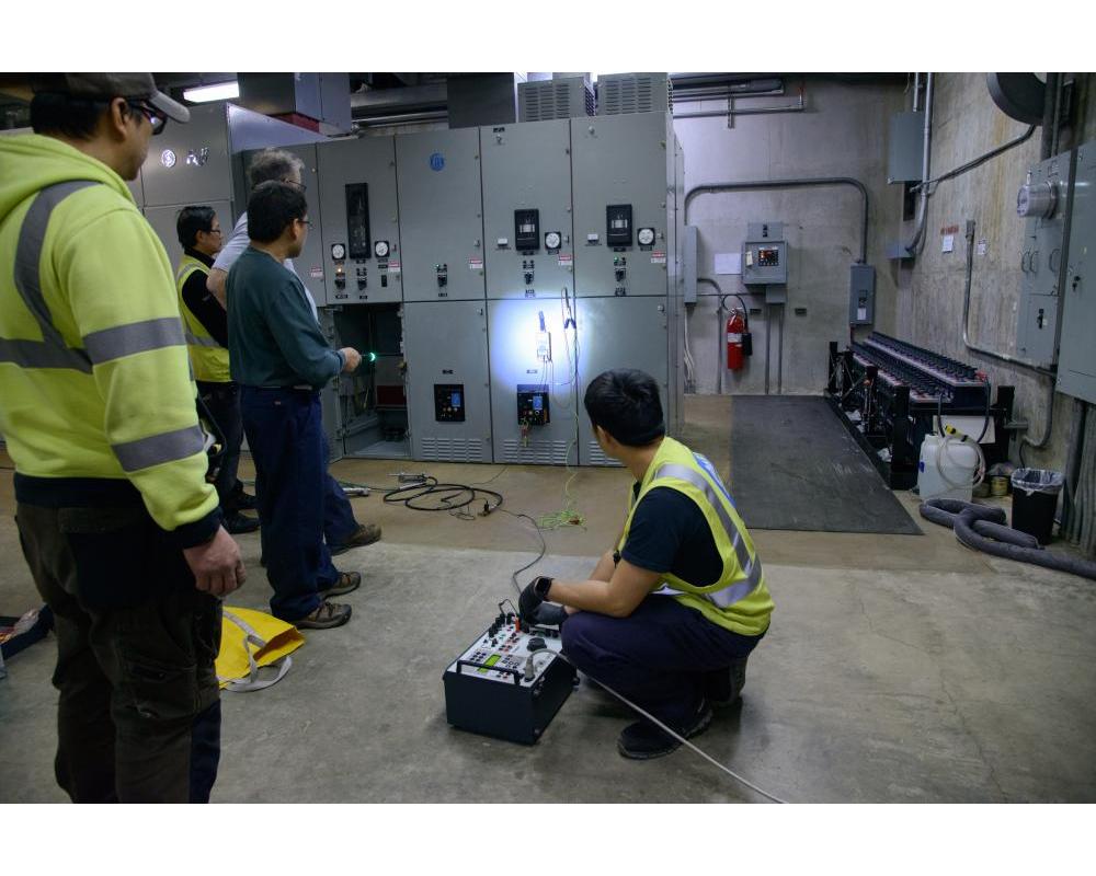 Several crew members inside a systems shop location looking at the cabinet wall. 
