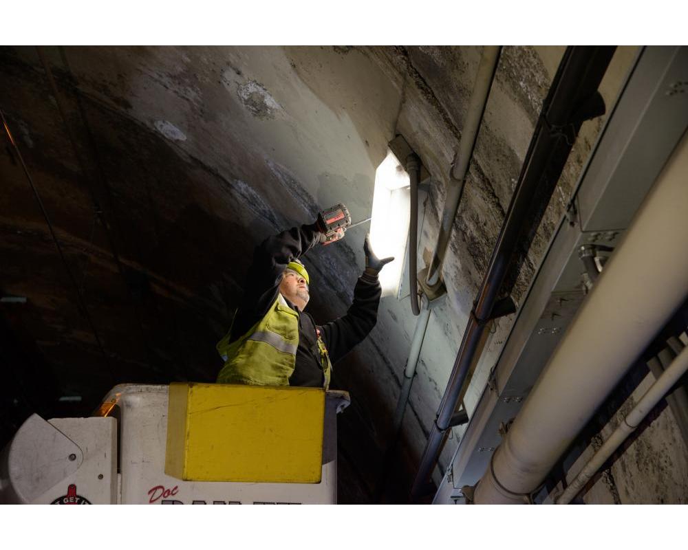 Crew member holding light by the tunnel ight. They seem to elevated by a lift. 