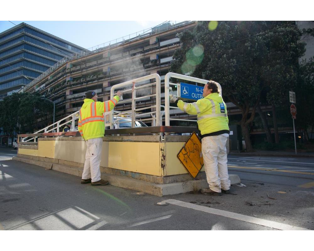 Two crew members by a wheelchair ramp with a building in the background.