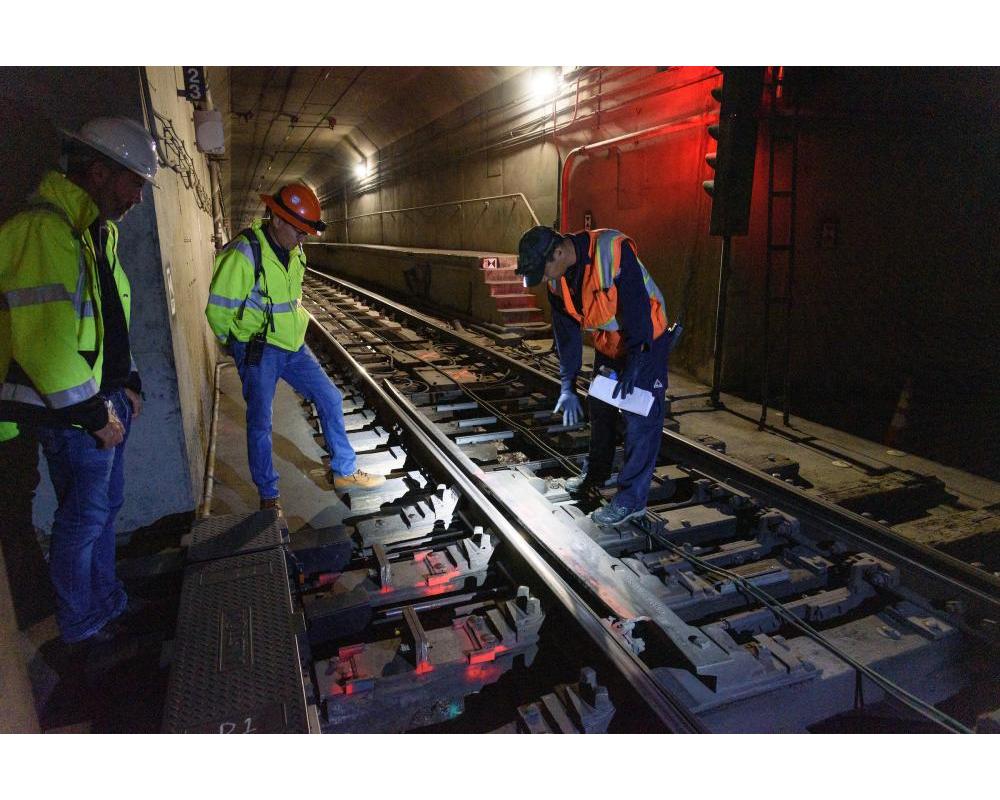 Workers looking at subway tracks and loop cable wire