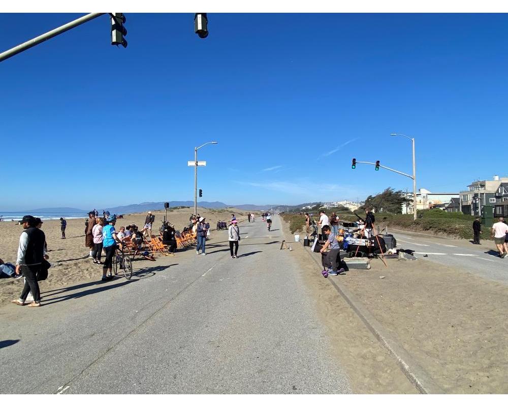 A road running alongside a beach with a crowd of people watching a band playing music.