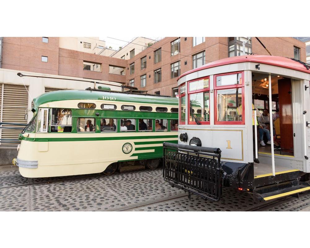 Two retro streetcars, one cream and green and one gray and red, pause during Muni Heritage Weekend 2023.
