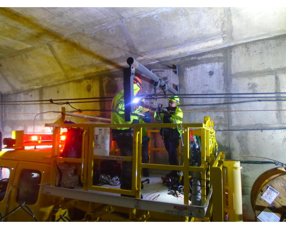Crews stand on a yellow elevated piece of equipment in a Muni Metro tunnel as they work on overhead wires.