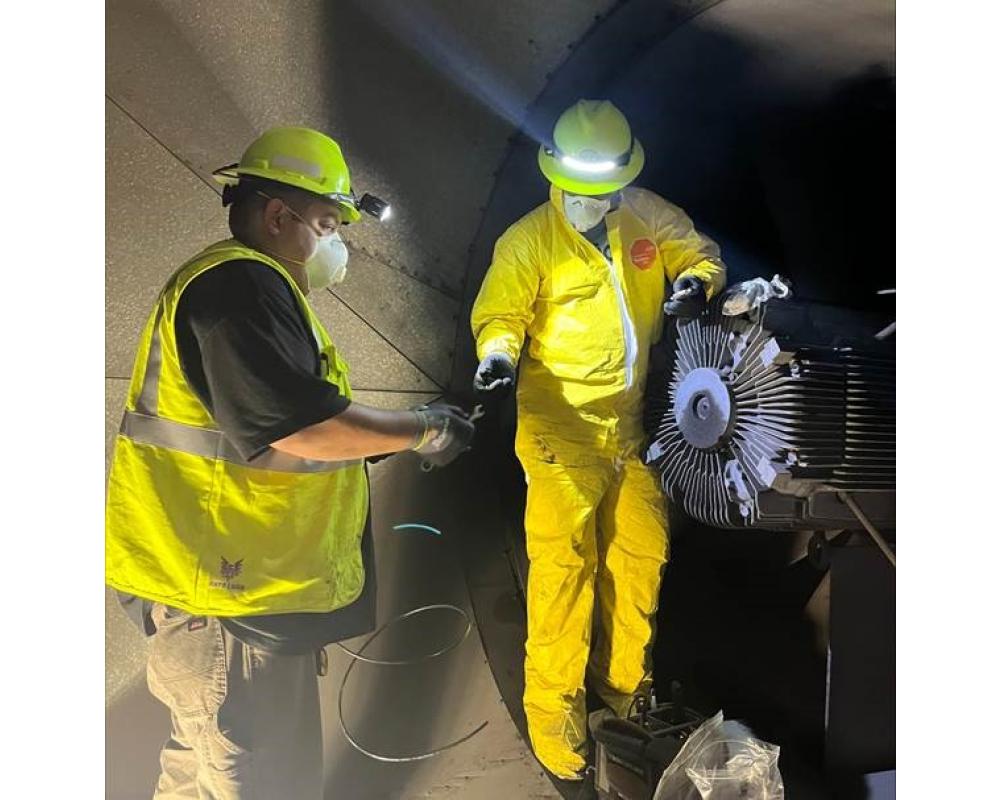 Two crew members in yellow safety equipment reroute a grease line in a Muni Metro tunnel for Fix-It Week.