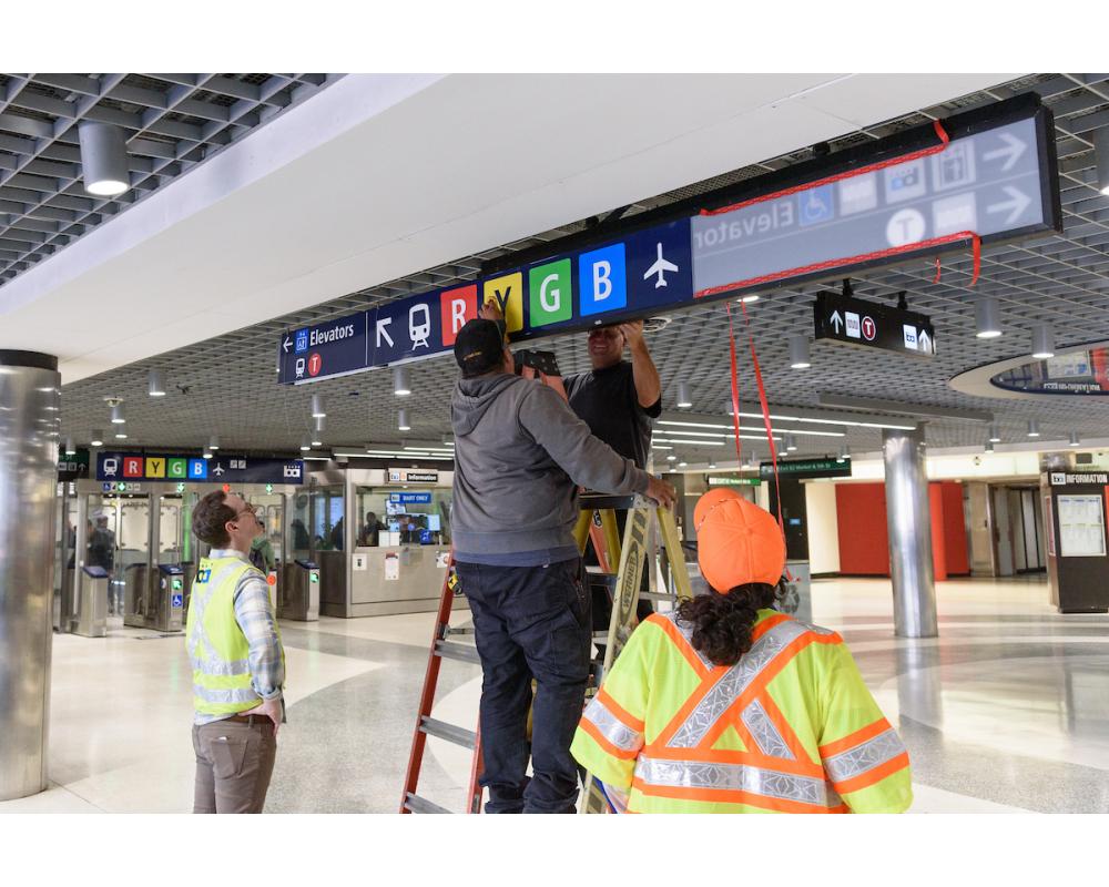 A photo of workers installing test signs at Powell Station for the Regional Mapping and Wayfinding Project.