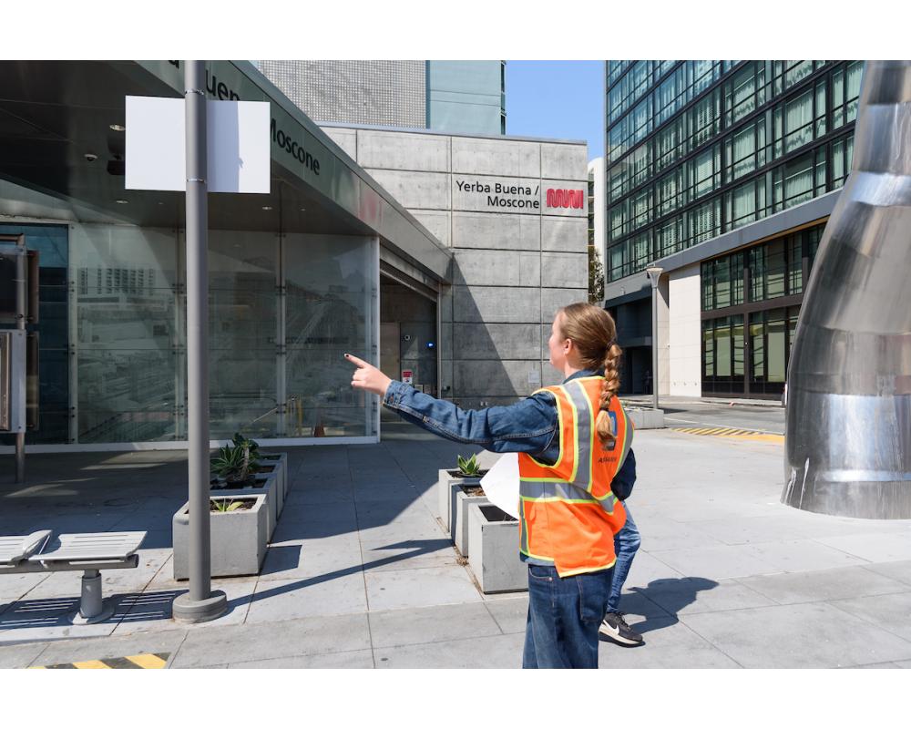 Intern pointing south at the Yerba Buena station entrance during site assessment.