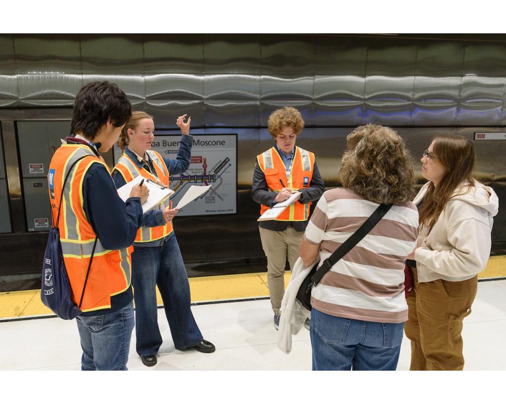 Three interns interviewing members of the public on a subway platform.