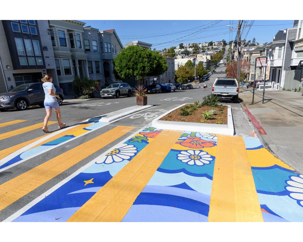 Person walks by a crosswalk that has a floral mural with multiple colors.