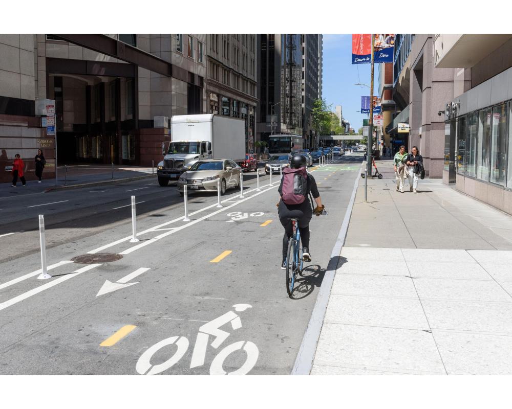 Person rides a bike on a separated bikeway that has hit-posts between the bikeway and moving vehicles.