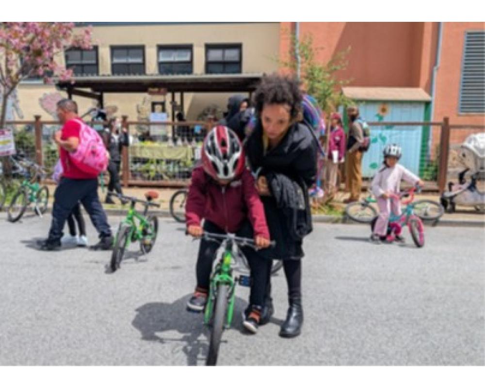 An adult helps a child balance on a bike in a school playground during an event.
