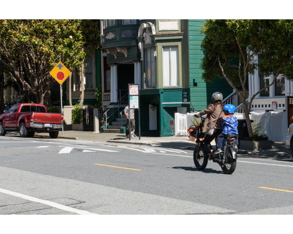Adult and child ride on a bike toward a speed hump. 