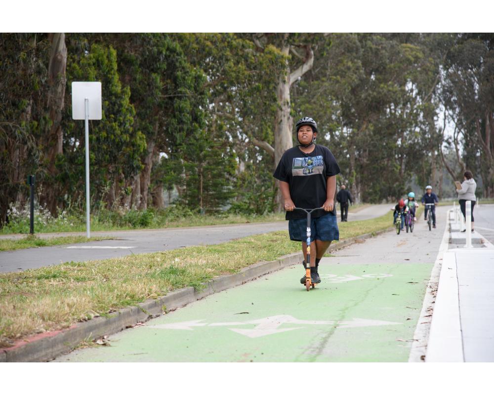 Youth riding a scooter on a green separated bikeway. 