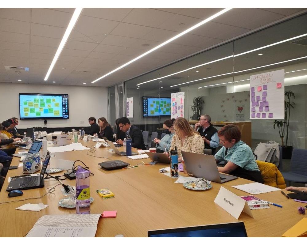 a group of people sitting at a conference table. The Working Group met the developer team in Dec 2022.
