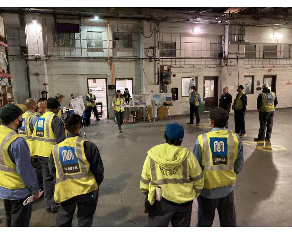 marintenance staff in yellow vests gather around a person speaking