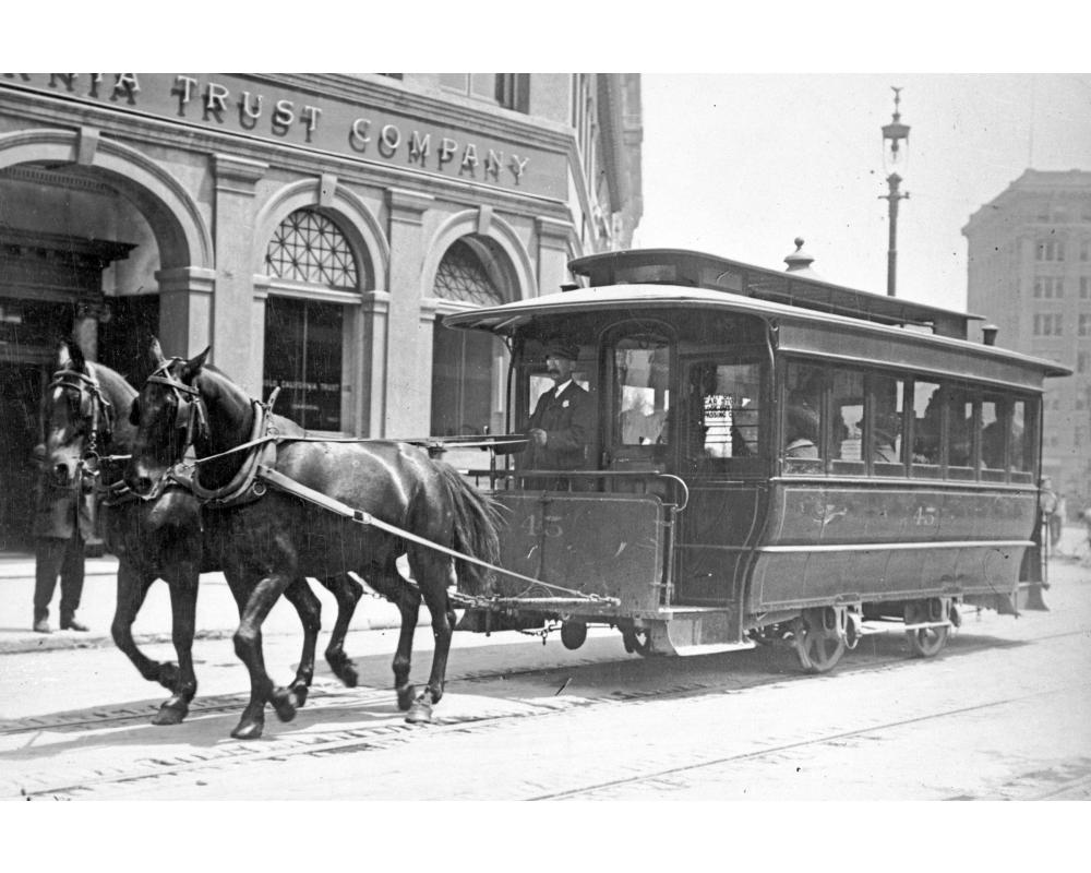 black and white photo of a horse-drawn streetcar in downtown san francisco in the late 1800s.