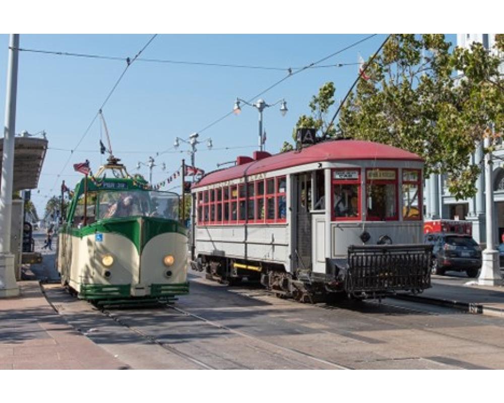 Two vintage streetcars next to each other on the street, one is open air with no roof.