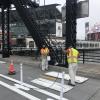 two people wearing yellow safety vests spray painting white paint using stencils in a two-way bikeway with plastic delineators