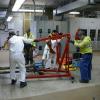 Several crew members holding a large device instrument inside a systems shop location. 