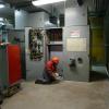 Two crew members in full protected wear inside a shops location. The walls are bordered with systems cabinets and decks. 