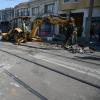 Excavator with extended arm and alongside the rail tracks and residential homes.