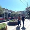 People walking by sidewalk planters near train. 